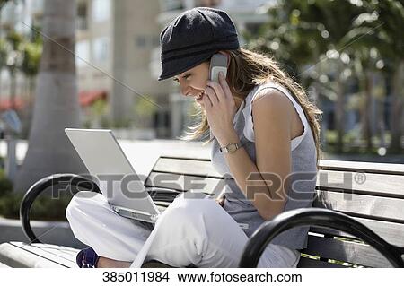 Young woman talking on a mobile phone and using a laptop View Large Photo Image Picture - Young woman talking on a mobile phone and using a laptop. Fotosearch