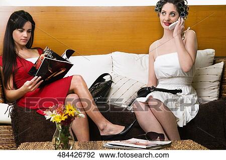 Stock Image - Young woman talking on a mobile phone with another young woman reading a book. Fotosearch