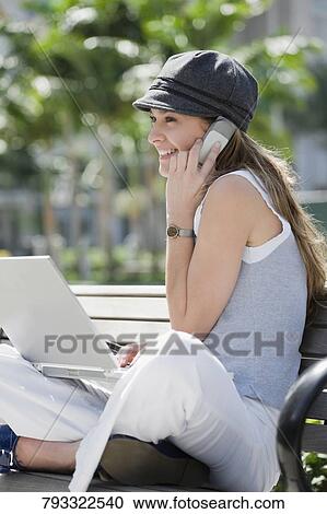 Young woman talking on a mobile phone and using a laptop View Large Photo Image Stock Image - Young woman talking on a mobile phone and using a laptop. Fotosearch