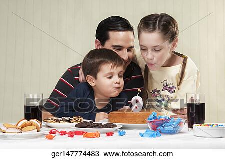 Stock Image - Boy and a girl blowing out birthday candles with their father. Fotosearch