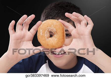 Boy holding a donut in front of his eye View Large Photo Image Stock Photo - Boy holding a donut in front of his eye. Fotosearch