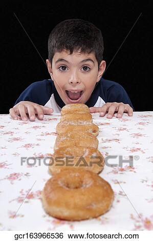 Boy with a row of donuts at a table View Large Photo Image Stock Photograph - Boy with a row of donuts at a table. Fotosearch