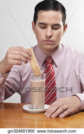 Stock Image - Businessman dipping a wafer into milk. Fotosearch
