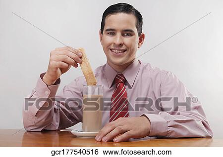 Businessman dipping a wafer into milk View Large Photo Image Stock Photograph - Businessman dipping a wafer into milk. Fotosearch