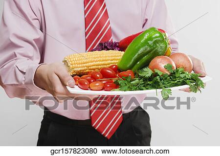 Stock Image - Businessman holding a platter of fresh vegetables. Fotosearch