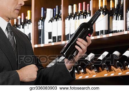 Businessman reading the label of a wine bottle View Large Photo Image Stock Image - Businessman reading the label of a wine bottle. Fotosearch