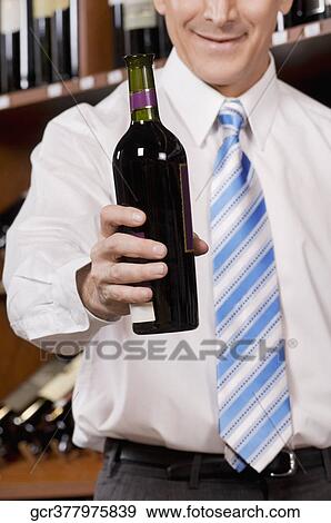 Stock Photo - Businessman showing a wine bottle in a bar. Fotosearch