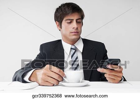 Businessman using a mobile phone over a cup of coffee View Large Photo Image Stock Photo - Businessman using a mobile phone over a cup of coffee. Fotosearch