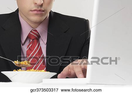 Stock Photo - Businessman working on a laptop at breakfast table. Fotosearch