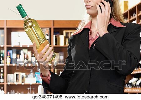 Businesswoman talking on a mobile phone and holding a wine bottle View Large Photo Image Stock Photograph - Businesswoman talking on a mobile phone and holding a wine bottle. Fotosearch