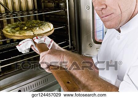 Chef putting a pizza into an oven View Large Photo Image Stock Photo - Chef putting a pizza into an oven. Fotosearch