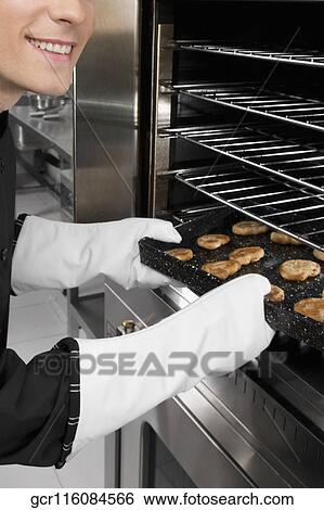 Chef taking out a tray of cookies from an oven View Large Photo Image Stock Photograph - Chef taking out a tray of cookies from an oven. Fotosearch