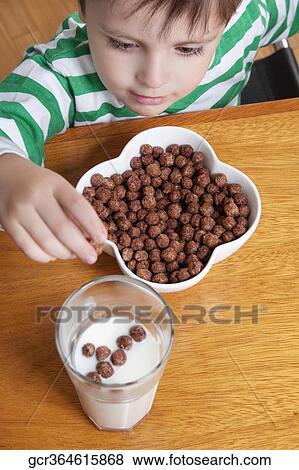 Close-up of a boy dropping dry cereal into a glass of milk View Large Photo Image Stock Photo - Close-up of a boy dropping dry cereal into a glass of milk. Fotosearch