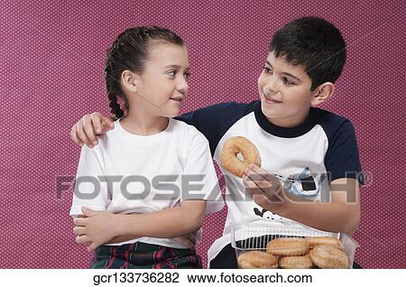 Stock Image - Close-up of a boy feeding a donut to his sister. Fotosearch