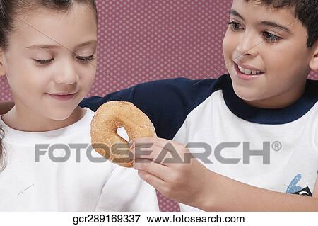 Stock Photo - Close-up of a boy feeding a donut to his sister. Fotosearch