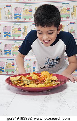 Stock Image - Close-up of a boy looking at a platter of nachos. Fotosearch