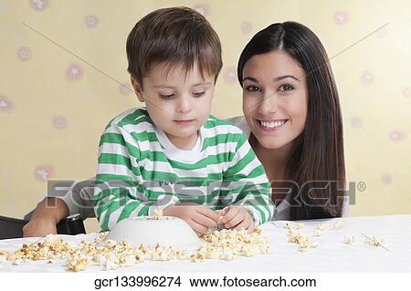 Close-up of a boy playing with popcorns beside his mother View Large Photo Image Picture - Close-up of a boy playing with popcorns beside his mother. Fotosearch