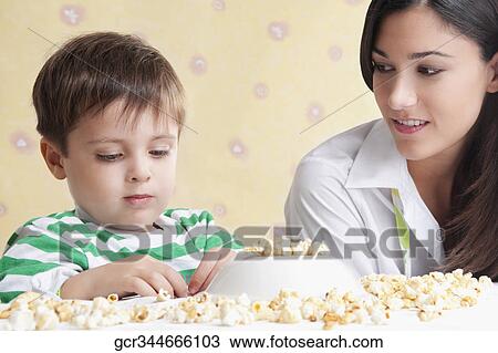 Close-up of a boy playing with popcorns beside his mother View Large Photo Image Stock Image - Close-up of a boy playing with popcorns beside his mother. Fotosearch