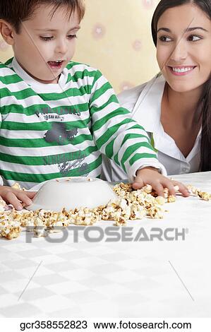 Close-up of a boy playing with popcorns beside his mother View Large Photo Image Stock Image - Close-up of a boy playing with popcorns beside his mother. Fotosearch