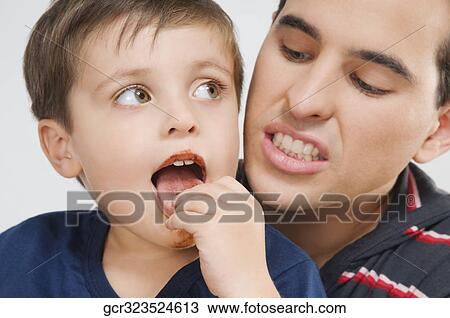 Close-up of a boy sitting in his father's lap and eating cookies View Large Photo Image Stock Image - Close-up of a boy sitting in his father's lap and eating cookies. Fotosearch