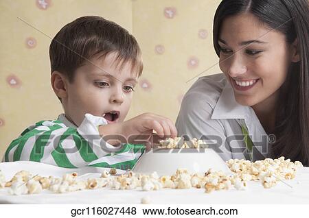 Close-up of a boy sitting with his mother and playing with popcorn View Large Photo Image Stock Photo - Close-up of a boy sitting with his mother and playing with popcorn. Fotosearch