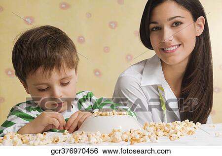 Close-up of a boy sitting with his mother and playing with popcorn View Large Photo Image Stock Photograph - Close-up of a boy sitting with his mother and playing with popcorn. Fotosearch