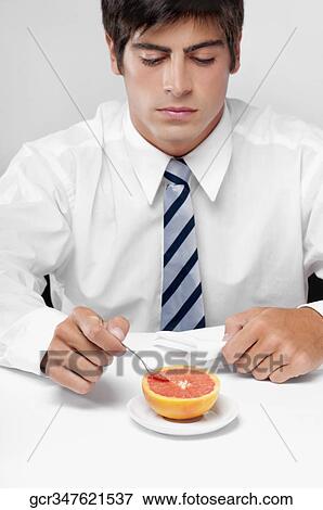 Close-up of a businessman eating a grapefruit with a spoon View Large Photo Image Stock Photo - Close-up of a businessman eating a grapefruit with a spoon. Fotosearch