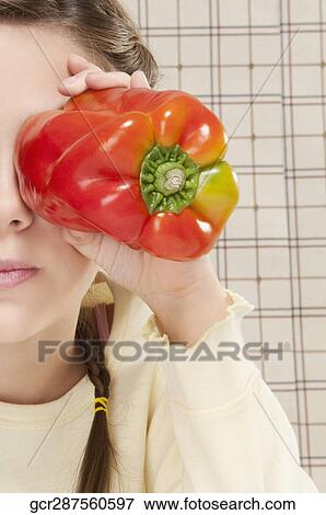 Stock Photo - Close-up of a girl holding bell pepper in front of her eyes. Fotosearch