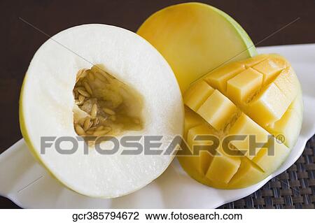 Stock Image - Close-up of a half of melon with a slice of mango. Fotosearch