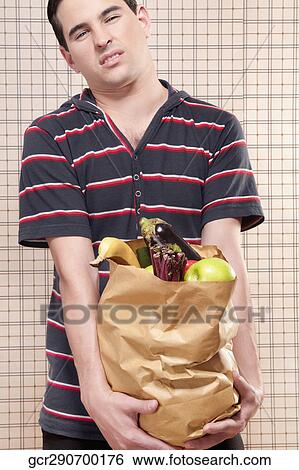 Close-up of a man holding a bag of fruits and vegetables View Large Photo Image Stock Photograph - Close-up of a man holding a bag of fruits and vegetables. Fotosearch