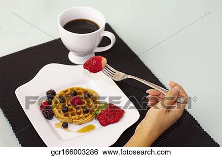 Stock Photograph - Close-up of a person holding a strawberry over waffles. Fotosearch