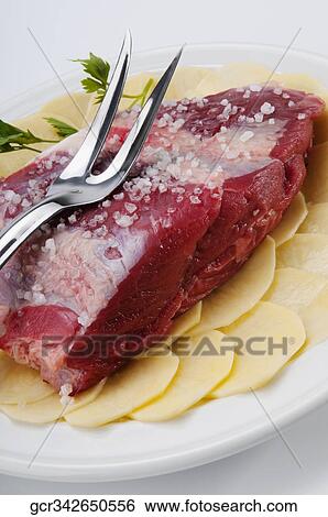 Close-up of a raw steak on a bed of sliced potatoes marinated with rock salt View Large Photo Image Stock Photograph - Close-up of a raw steak on a bed of sliced potatoes marinated with rock salt. Fotosearch
