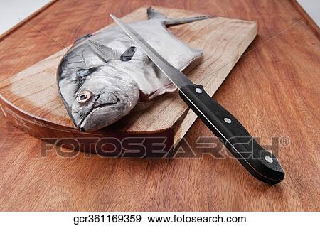 Stock Photo - Close-up of a whole raw fish with a knife. Fotosearch