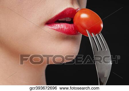 Stock Photograph - Close-up of a woman eating a cherry tomato. Fotosearch