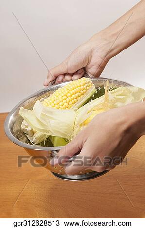 Stock Image - Close-up of corn in a colander in a person's hands. Fotosearch