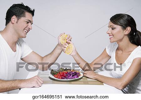 Stock Image - Couple squeezing orange halves over a salad. Fotosearch