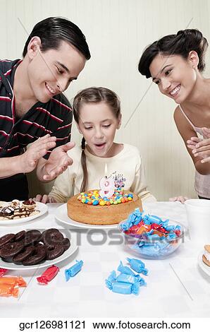 Stock Image - Girl blowing out birthday candle with their parents. Fotosearch