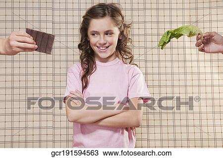 Stock Image - Girl choosing between a chocolate and a lettuce leaf. Fotosearch