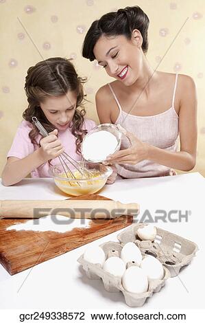 Stock Image - Girl helping her mother in cooking. Fotosearch