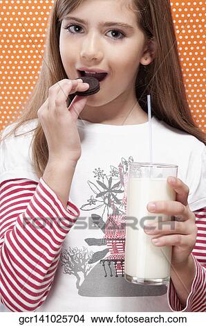 Picture - Girl holding a glass of milk and eating a cookie. Fotosearch