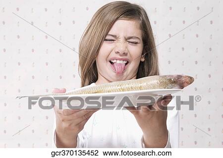 Girl holding a raw fish on a plate and making a disgust face View Large Photo Image Stock Image - Girl holding a raw fish on a plate and making a disgust face. Fotosearch