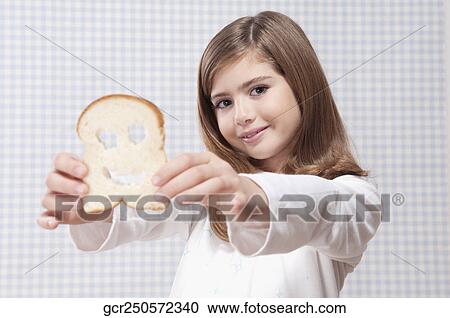 Stock Image - Girl holding a slice of bread with smiley face. Fotosearch