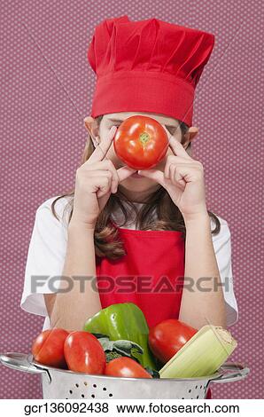 Girl holding a tomato in front of her face View Large Photo Image Stock Photo - Girl holding a tomato in front of her face. Fotosearch