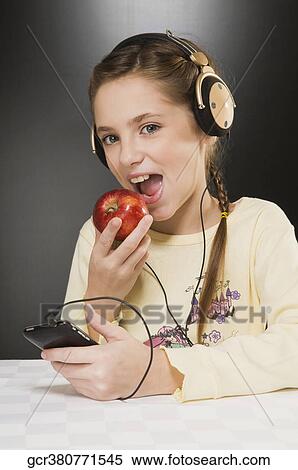 Girl listening to music and eating an apple View Large Photo Image Stock Photography - Girl listening to music and eating an apple. Fotosearch