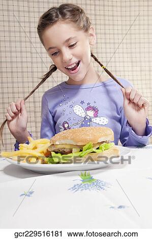 Stock Image - Girl looking at a plate of burger and French fries. Fotosearch