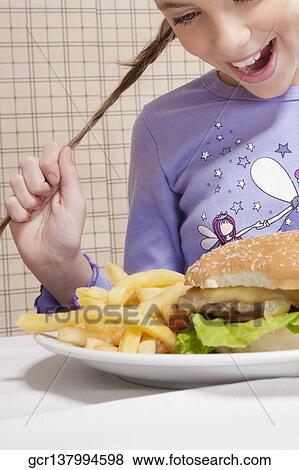 Girl looking at a plate of burger and French fries View Large Photo Image Stock Photo - Girl looking at a plate of burger and French fries. Fotosearch