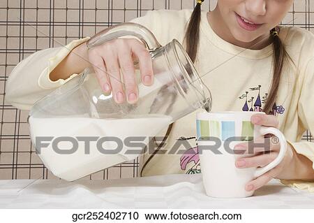 Stock Image - Girl pouring milk into a cup. Fotosearch