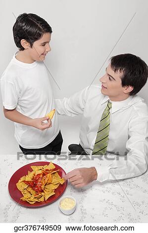 Man and his son eating nachos with salsa View Large Photo Image Stock Photo - Man and his son eating nachos with salsa. Fotosearch