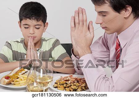 Stock Photograph - Man and his son praying before lunch. Fotosearch