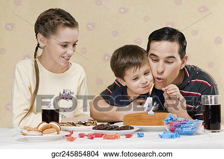 Man blowing out birthday candle with his son and daughter View Large Photo Image Picture - Man blowing out birthday candle with his son and daughter. Fotosearch